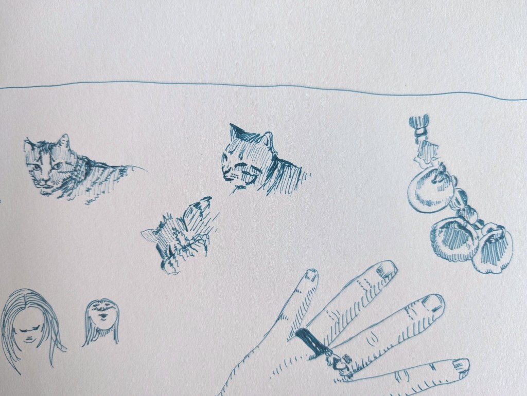 Various pen sketches on paper including cats, a hand, a segment of a bracelet and some small woman's faces